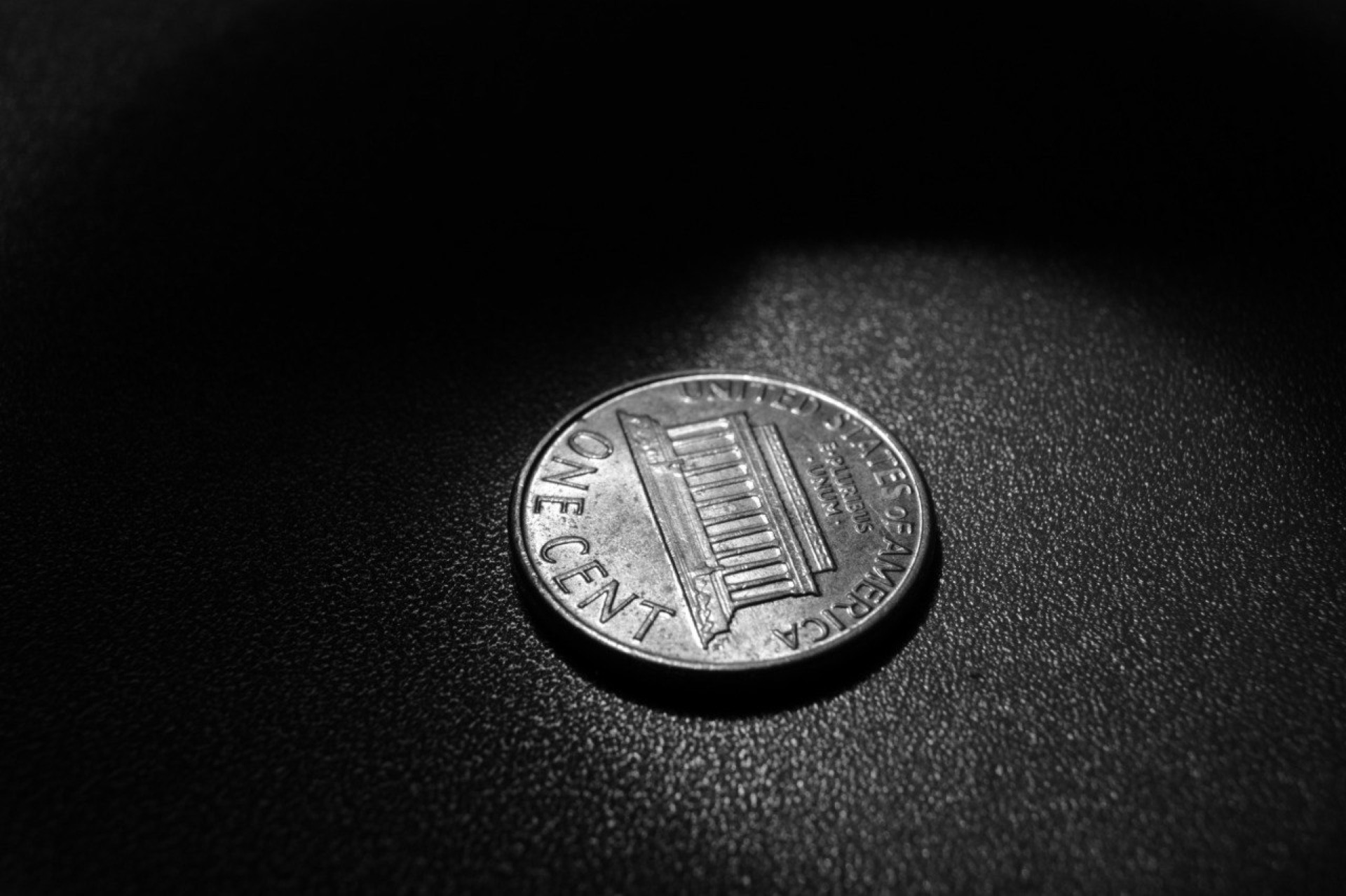 Close-up black-and-white photo of a U.S. one-cent coin on a dark textured surface, Lincoln Memorial side visible